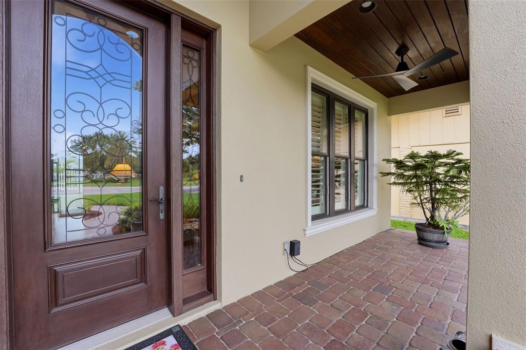 A covered brick porch features a wooden front door with glass panels and a ceiling fan — 424 PENSACOLA ROAD, VENICE, FL