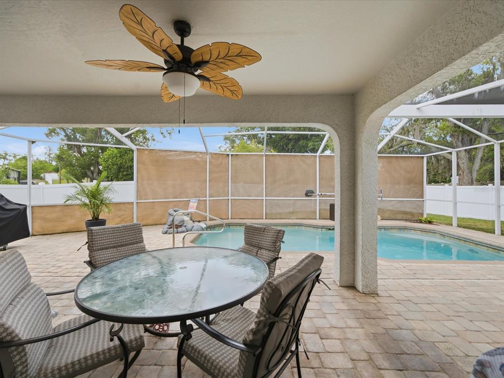 A covered patio features a glass-top dining set, a ceiling fan, and a screened pool — 2478 GLENRIDGE DR, SPRING HILL, FL