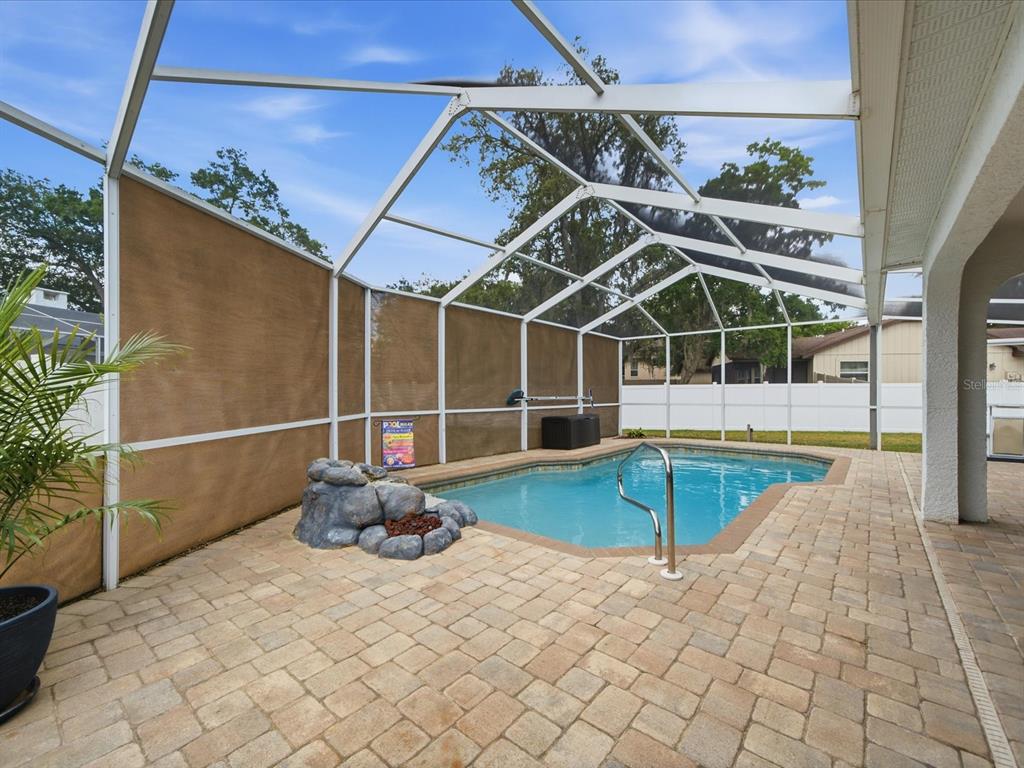 A screened-in pool area features a paver patio, a small rock fountain, and a pool — 2478 GLENRIDGE DR, SPRING HILL, FL