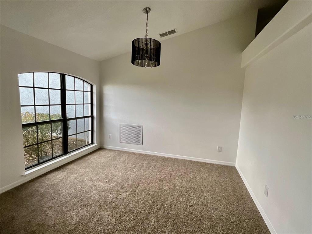 An empty room with beige carpet, white walls, a vaulted ceiling, and a black chandelier — 511 COVENTRY ROAD, DAVENPORT, FL