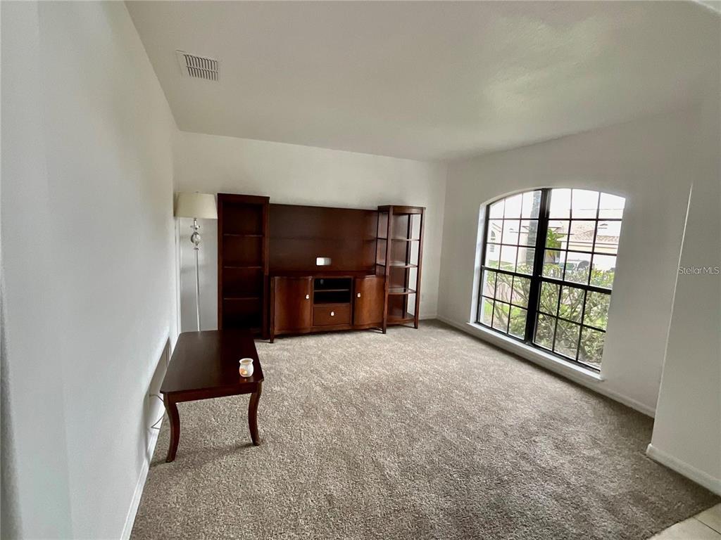 A carpeted living room features a wooden media center, a side table, and an arched window — 511 COVENTRY ROAD, DAVENPORT, FL