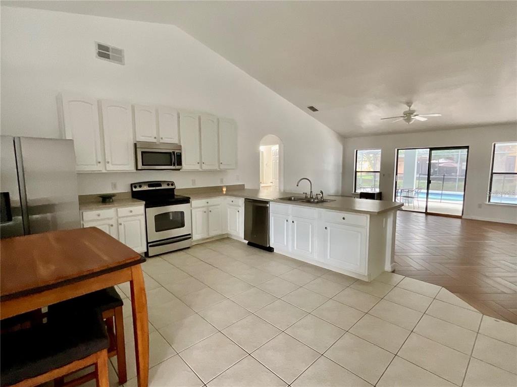 A kitchen with white cabinets, stainless steel appliances, and tile flooring opens to a living area — 511 COVENTRY ROAD, DAVENPORT, FL