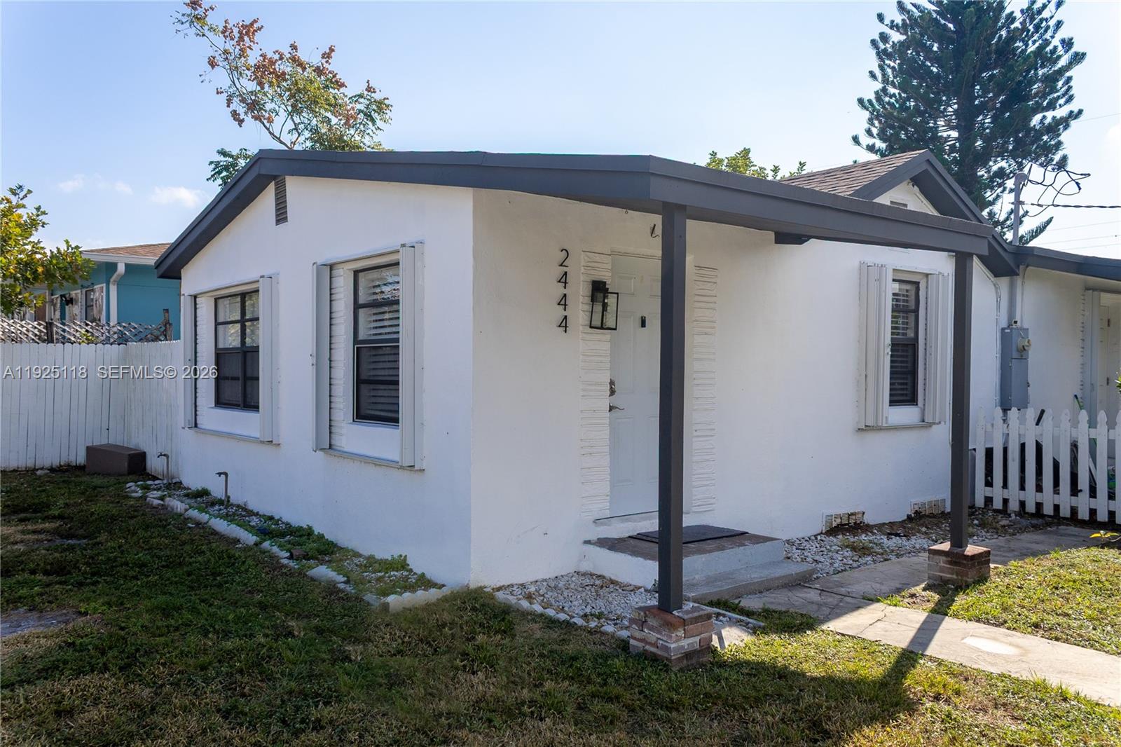 A white, single-story house features a dark-trimmed porch, a front door, and a white fence — 2444 Roosevelt St, Hollywood FL 33020, HOLLYWOOD, FL