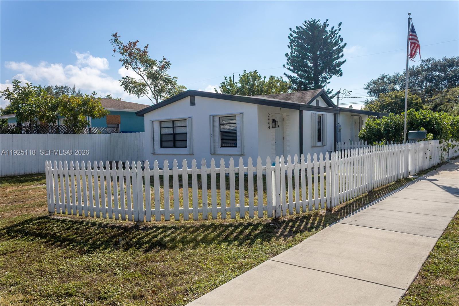 A white single-story house with a picket fence stands next to a sidewalk — 2444 Roosevelt St, Hollywood FL 33020, HOLLYWOOD, FL
