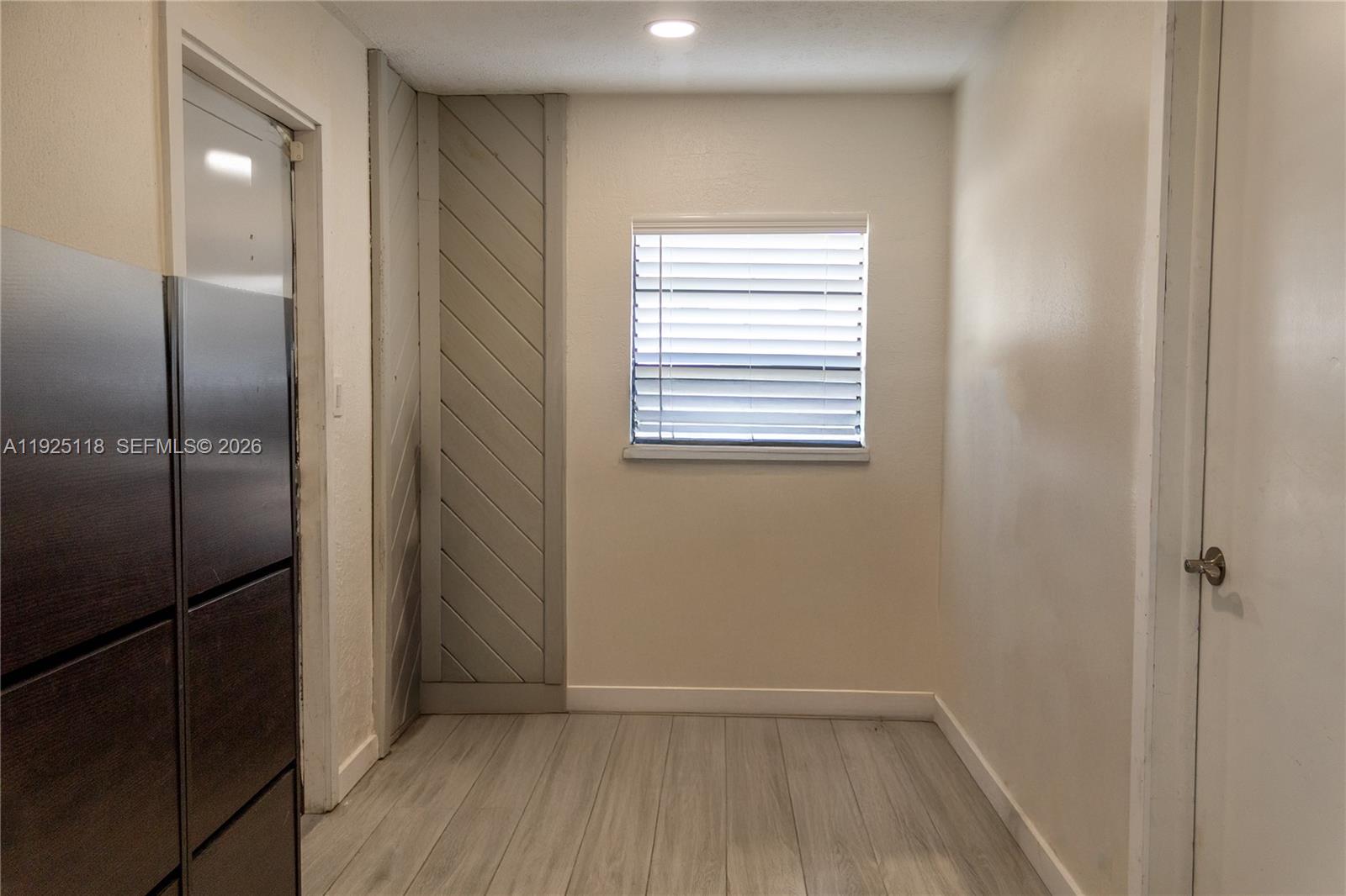 A small room features light wood-look flooring, a window with blinds, and diagonal wall paneling — 2444 Roosevelt St, Hollywood FL 33020, HOLLYWOOD, FL