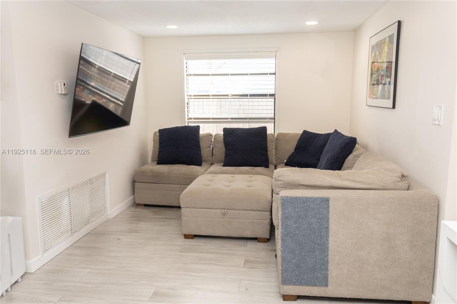 A living room features a beige sectional sofa, a wall-mounted television, and light wood flooring — 2444 Roosevelt St, Hollywood FL 33020, HOLLYWOOD, FL