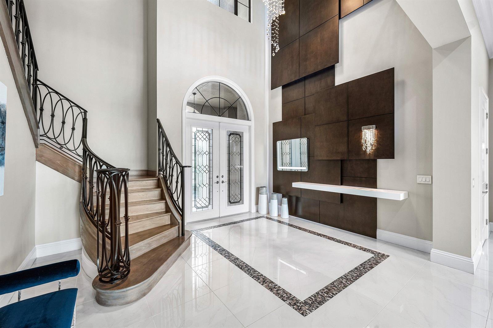 A grand foyer features a curved staircase, tiled floors, and a dark wood paneled wall — 9616 Moritz Way, Delray Beach FL 33446, DELRAY BEACH, FL