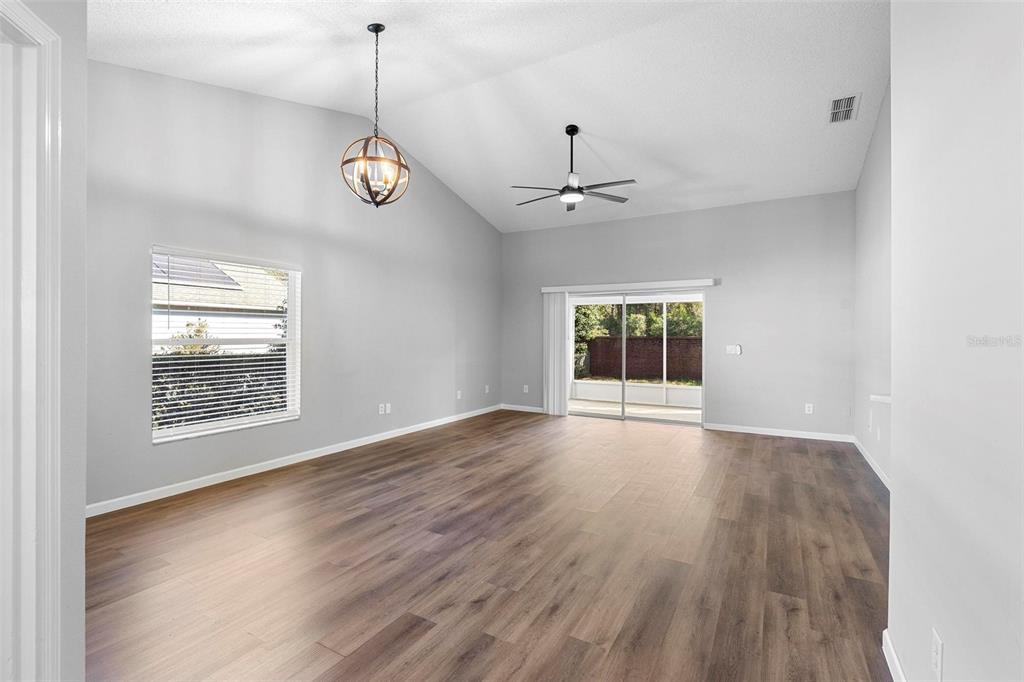 An empty living room features vaulted ceilings, wood-look flooring, a ceiling fan, and sliding doors — 846 GRAND HUGHEY COURT, APOPKA, FL