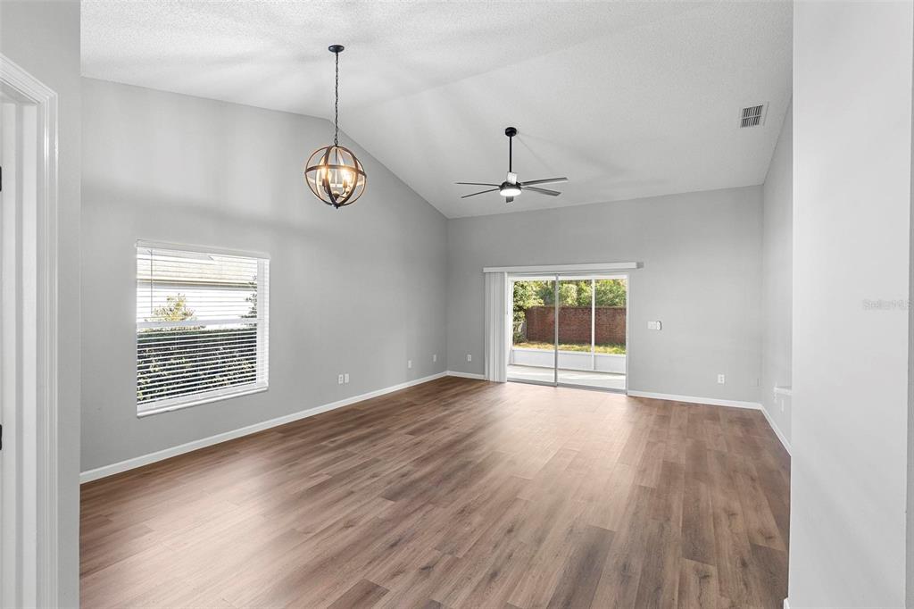 An empty living room features vaulted ceilings, wood-look flooring, a ceiling fan, and sliding doors — 846 GRAND HUGHEY COURT, APOPKA, FL