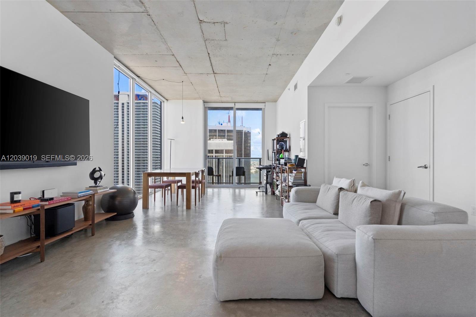 A modern living room features a concrete ceiling, polished floors, floor-to-ceiling windows, and city views — 151 SE 1st St # 3102, Miami FL 33131, MIAMI, FL