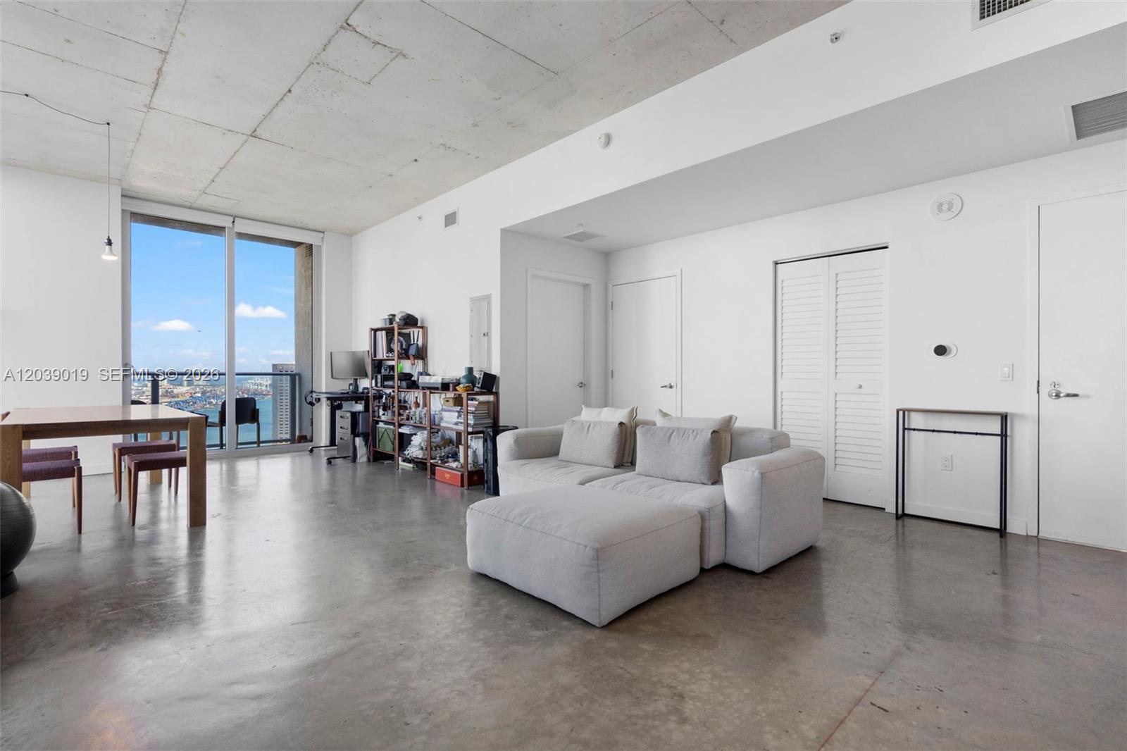 A modern living room features concrete floors, a raw concrete ceiling, and floor-to-ceiling windows — 151 SE 1st St # 3102, Miami FL 33131, MIAMI, FL