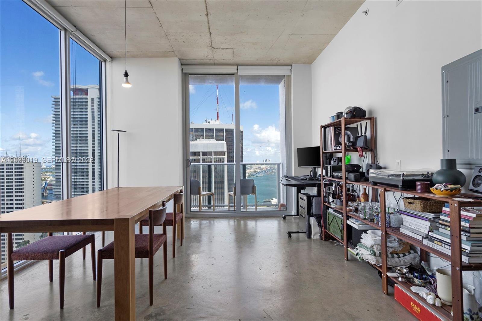 A modern apartment dining area features concrete ceilings, floor-to-ceiling windows, and a balcony with views — 151 SE 1st St # 3102, Miami FL 33131, MIAMI, FL