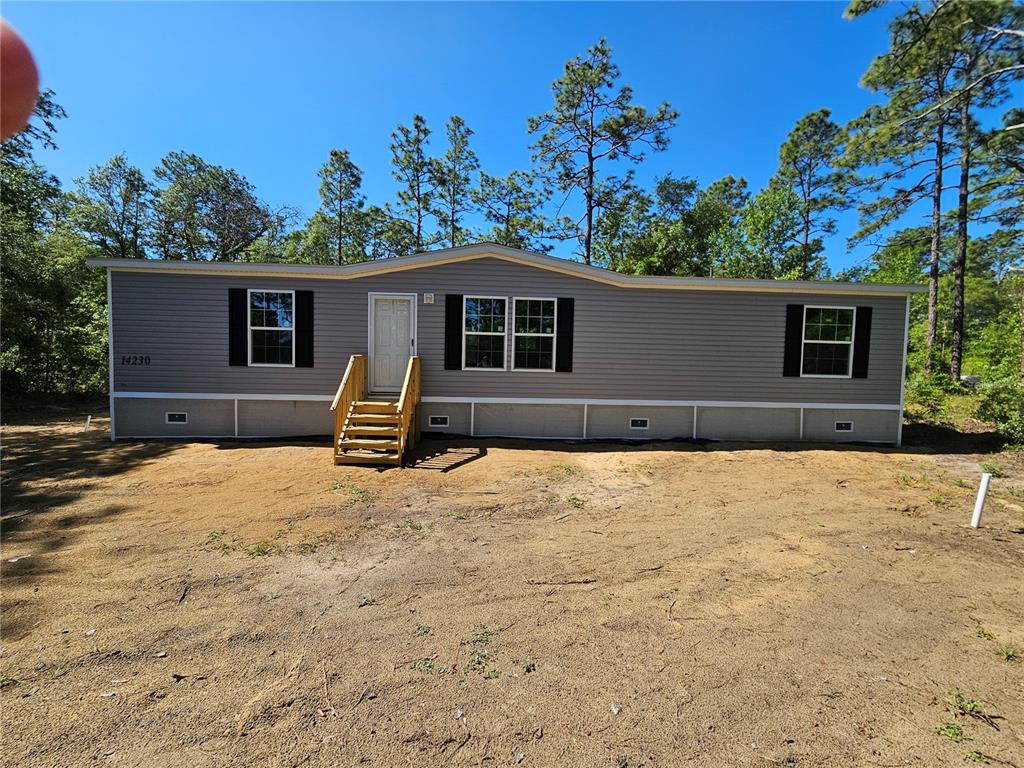 A single-story manufactured home with grey siding and wooden stairs sits on a dirt lot — 14230 SE 20TH STREET, MORRISTON, FL