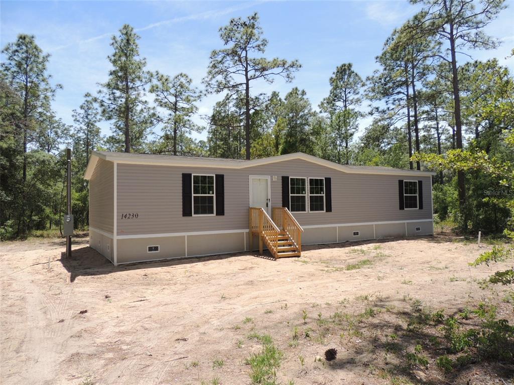 A tan manufactured home with a wooden staircase sits on a sandy lot — 14230 SE 20TH STREET, MORRISTON, FL