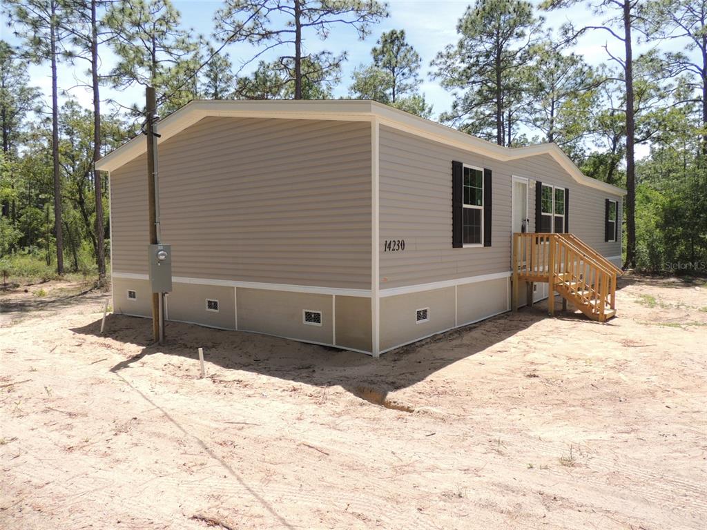 A gray manufactured home with a wooden staircase sits on a sandy, wooded lot — 14230 SE 20TH STREET, MORRISTON, FL