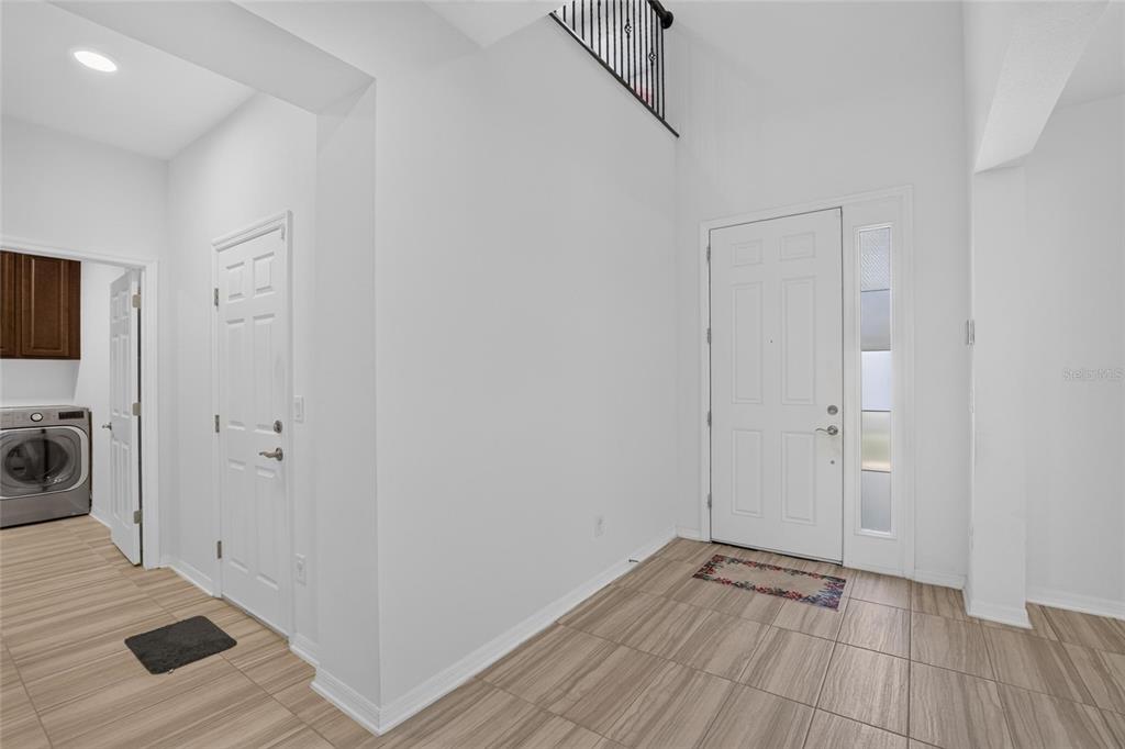 An entryway with tiled flooring, a white front door, and an adjacent laundry room — 7321 GULF CYPRESS AVENUE, LAND O LAKES, FL