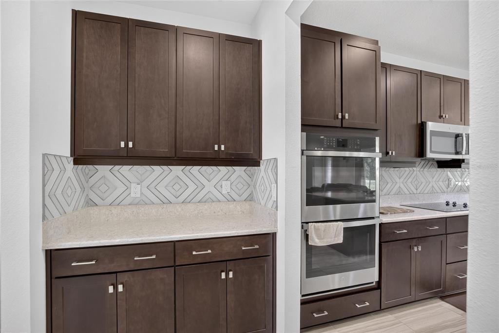 A kitchen features dark wood cabinets, light countertops, and a geometric patterned tile backsplash — 7321 GULF CYPRESS AVENUE, LAND O LAKES, FL
