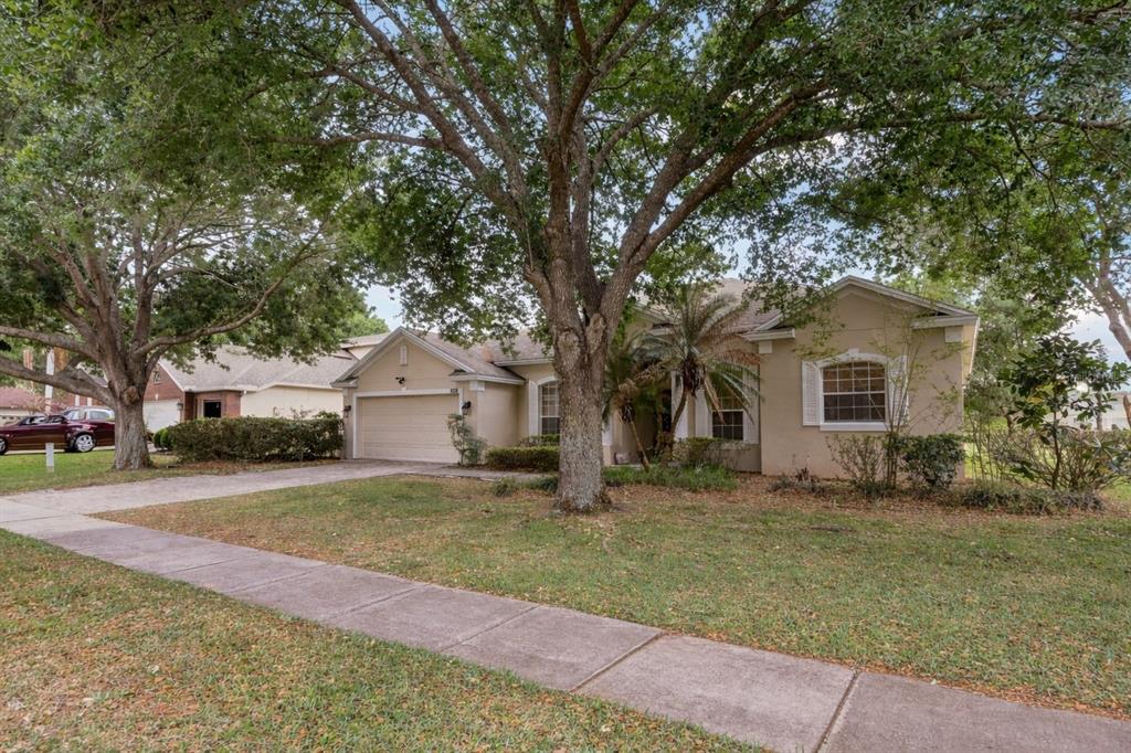 A single-story tan house with a two-car garage and large trees in the front yard — 3848 LONG BRANCH LANE, APOPKA, FL
