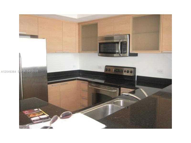 A kitchen features light wood cabinets, black countertops, stainless steel appliances, and a double sink — 140 S DIXIE HY # 502, Hollywood FL 33020, HOLLYWOOD, FL