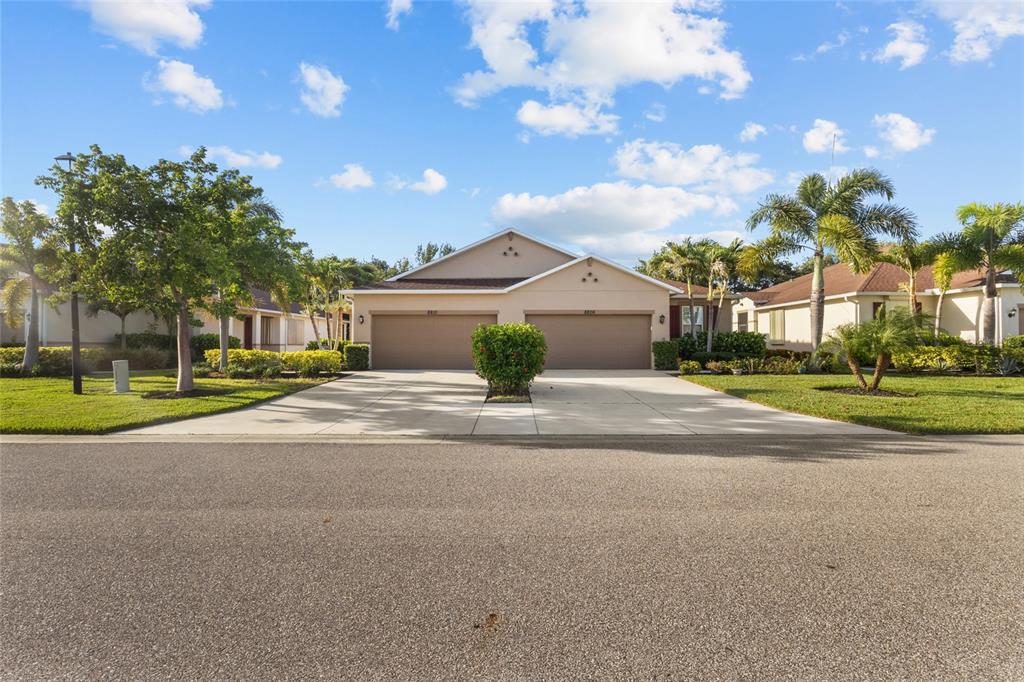 A single-story duplex home with two garage doors and a central bush in the driveway — 8810 TUSCANY ISLES DRIVE, PUNTA GORDA, FL