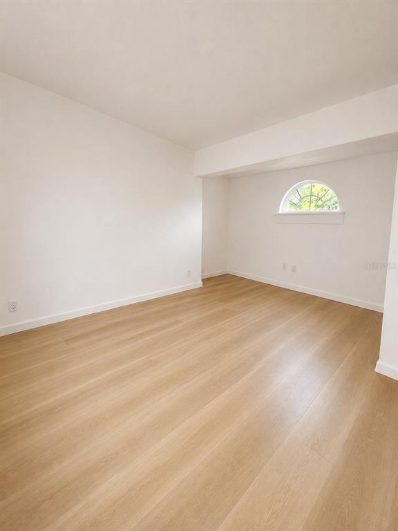 An empty room features light wood-look flooring, white walls, and a small arched window — 2827 S PARK AVENUE, SANFORD, FL