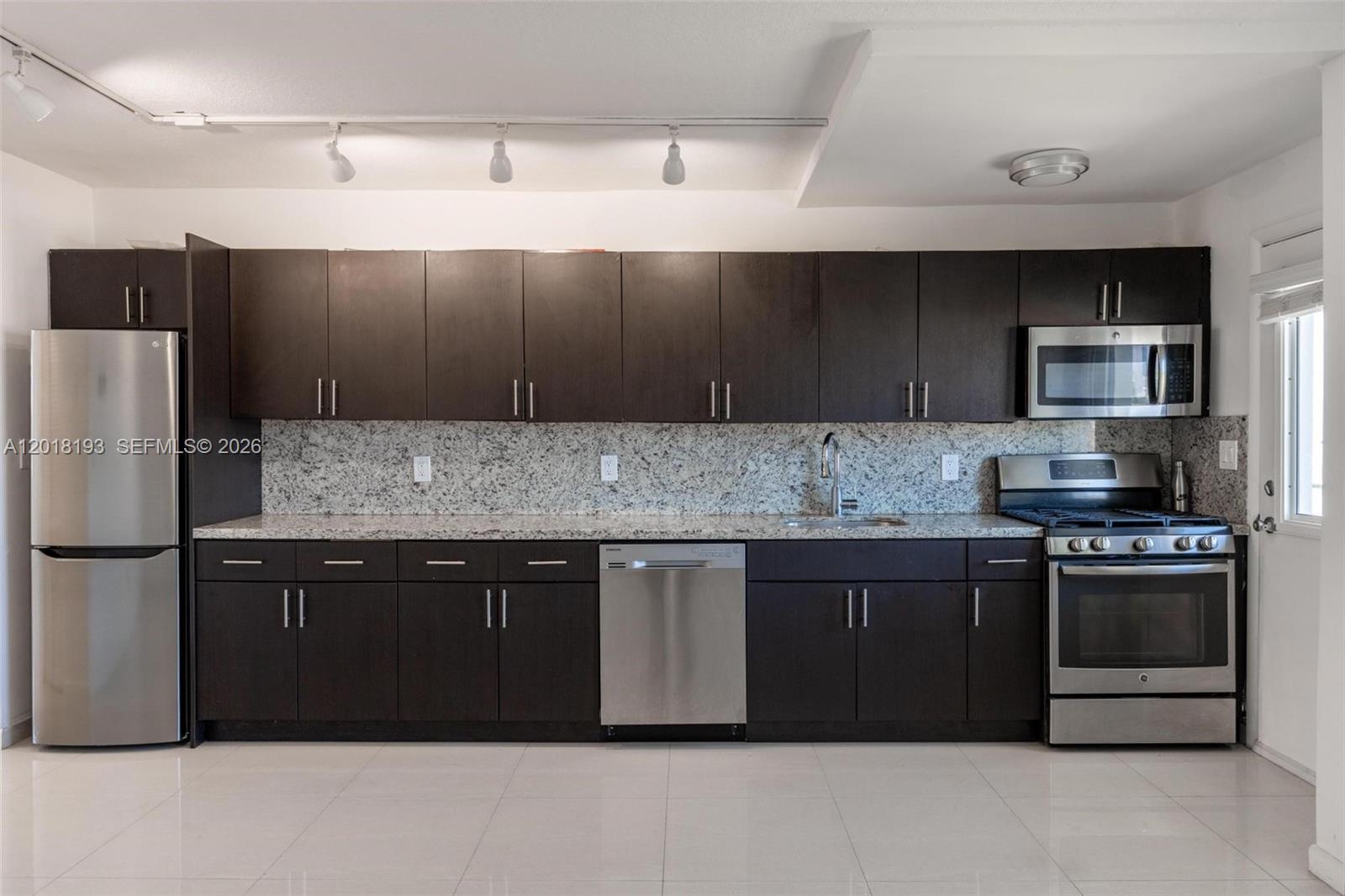 A kitchen features dark wood cabinets, stainless steel appliances, and speckled granite countertops — 525 Meridian Ave # 305, Miami Beach FL 33139, MIAMI BEACH, FL