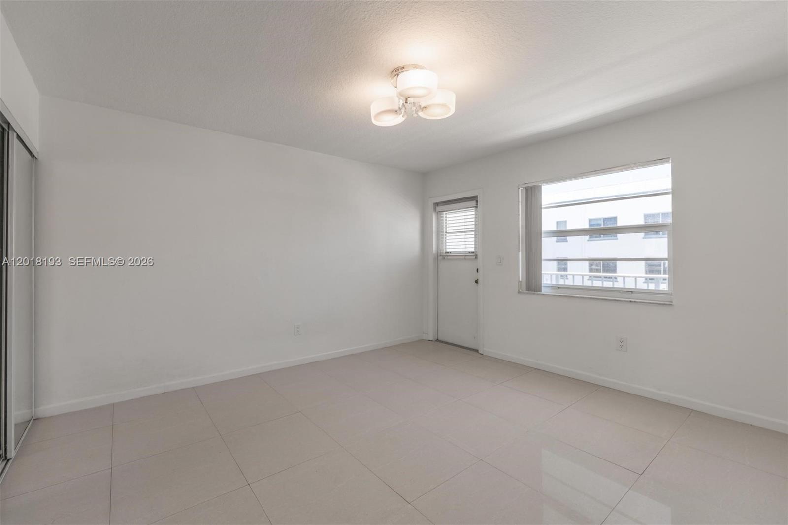 An empty room features white walls, light-colored tile flooring, a ceiling light, and a door — 525 Meridian Ave # 305, Miami Beach FL 33139, MIAMI BEACH, FL
