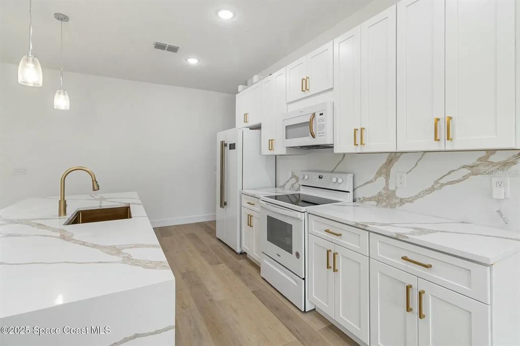 A modern kitchen features white cabinets, gold hardware, and a marble-patterned island with a sink — 435 GOLDSMITH AVENUE NW, PALM BAY, FL