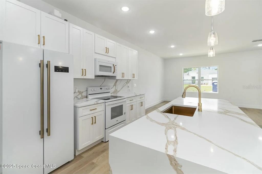 A modern kitchen features white cabinetry, a marble-patterned island, and gold-toned hardware — 435 GOLDSMITH AVENUE NW, PALM BAY, FL