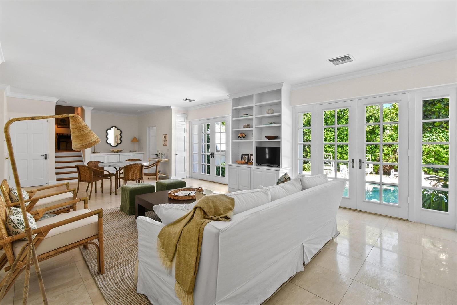 A bright living room features white built-in shelving, a sofa, and French doors overlooking a pool — 117 Via Vizcaya, Palm Beach FL 33480, PALM BEACH, FL