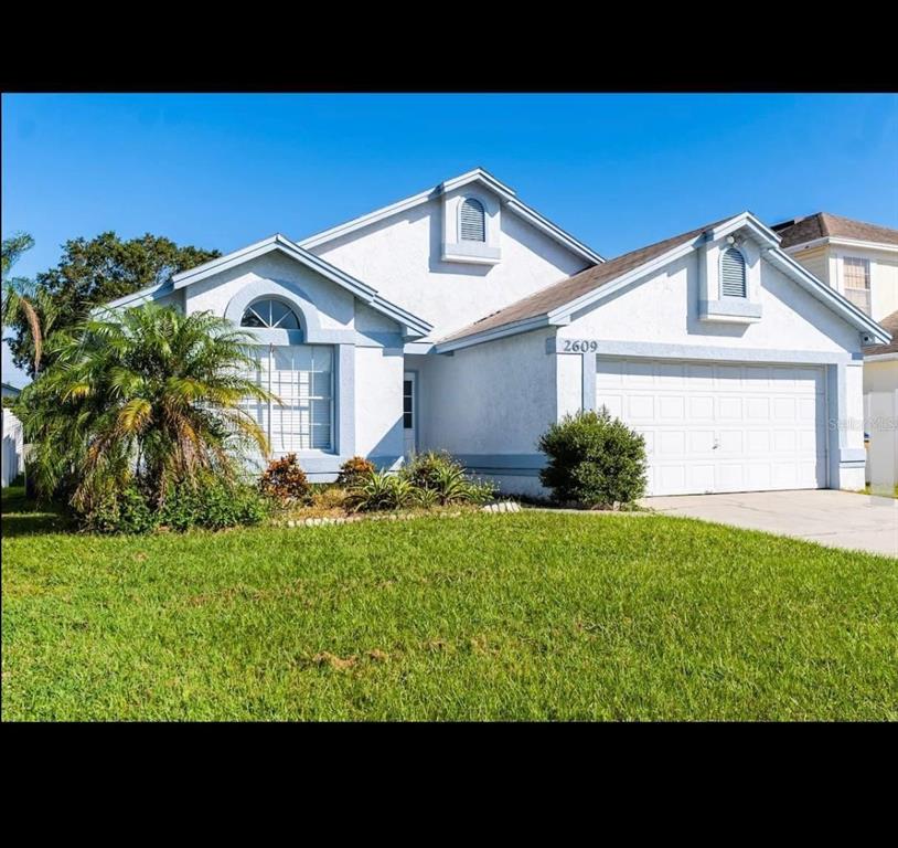 A single-story suburban house with a white stucco exterior, a two-car garage, and a lawn — 2609 MONTEGO BAY BOULEVARD, KISSIMMEE, FL
