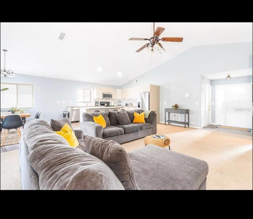 A living room with gray sofas, a ceiling fan, and an open kitchen in the background — 2609 MONTEGO BAY BOULEVARD, KISSIMMEE, FL
