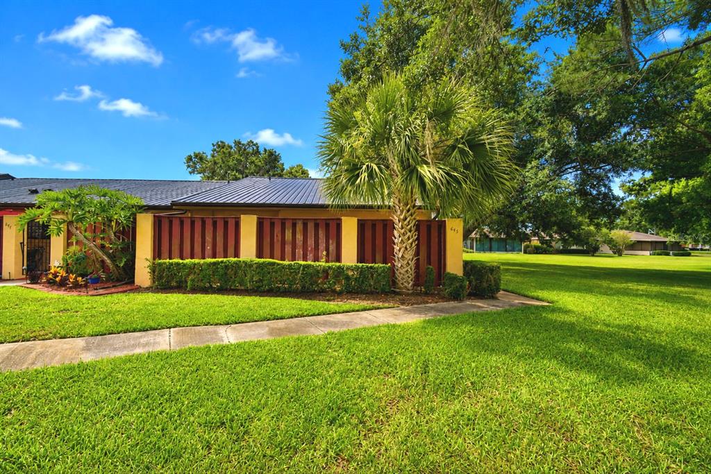 A palm tree stands in front of a house with a red fence and lawn — 645 BROADMOOR CIRCLE UNIT 645, WINTER HAVEN, FL