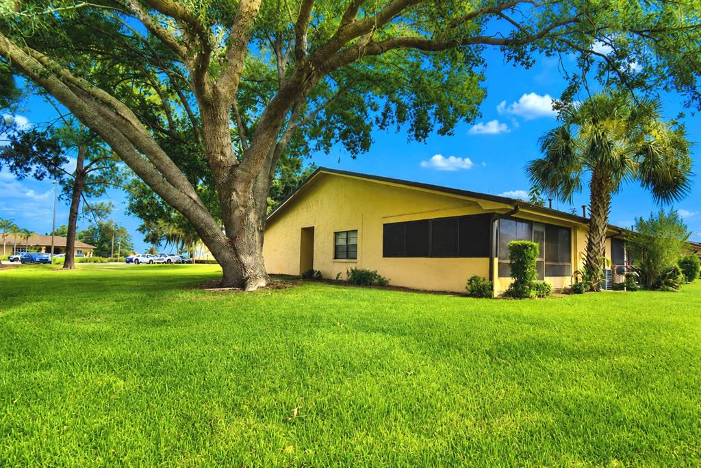 A yellow single-story building sits on a grassy lawn beneath a large oak tree — 645 BROADMOOR CIRCLE UNIT 645, WINTER HAVEN, FL