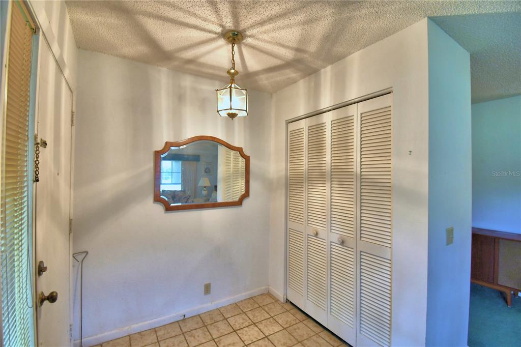 An entryway features tiled flooring, a hanging light fixture, a wall mirror, and bi-fold closet doors — 645 BROADMOOR CIRCLE UNIT 645, WINTER HAVEN, FL