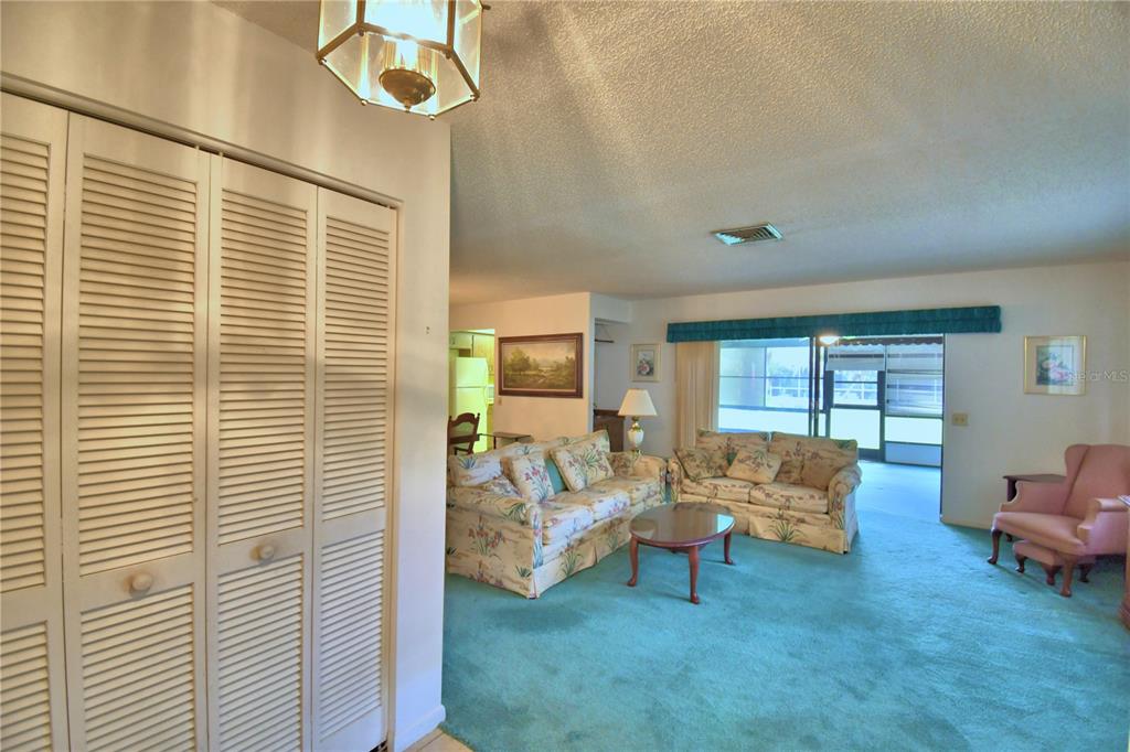 A living room features teal carpeting, floral sofas, a pink armchair, and louvered closet doors — 645 BROADMOOR CIRCLE UNIT 645, WINTER HAVEN, FL