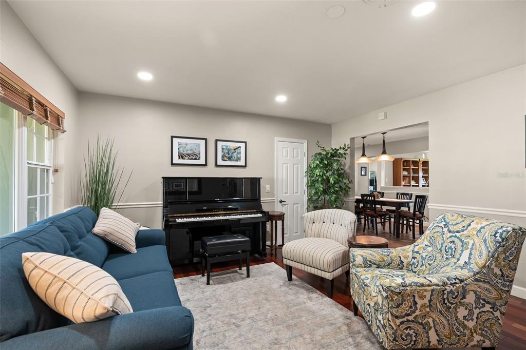 A living room features a blue sofa, a black piano, and two patterned accent chairs — 616 BRECHIN DRIVE, WINTER PARK, FL