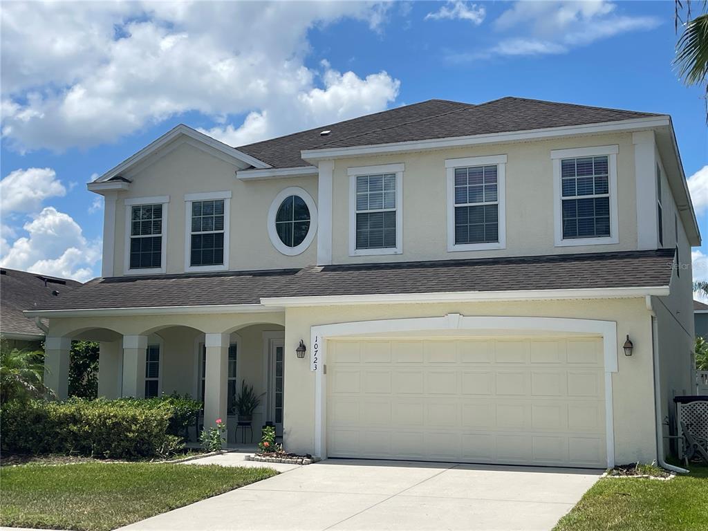 A two-story house with a beige stucco exterior, a two-car garage, and a covered porch — 10723 CLOVER WALK DRIVE, ORLANDO, FL