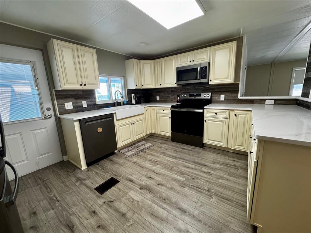 A kitchen features cream cabinets, dark appliances, a farmhouse sink, and wood-look flooring — 5619 BAYSHORE ROAD UNIT 120, PALMETTO, FL