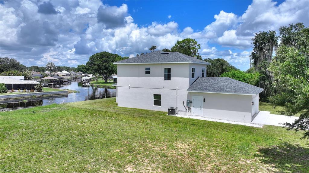 An exterior view of a two-story house with a white stucco finish near a canal — 100 TUOMEY COURT, LAKE PLACID, FL