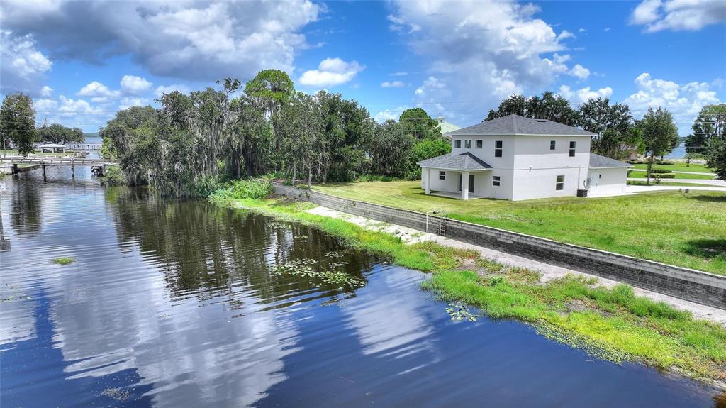 A two-story white house sits beside a canal with a stone retaining wall and trees — 100 TUOMEY COURT, LAKE PLACID, FL