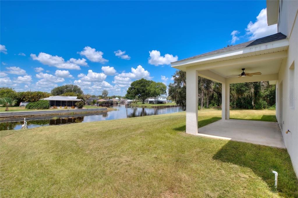 A covered patio overlooks a grassy backyard and a canal with neighboring houses — 100 TUOMEY COURT, LAKE PLACID, FL