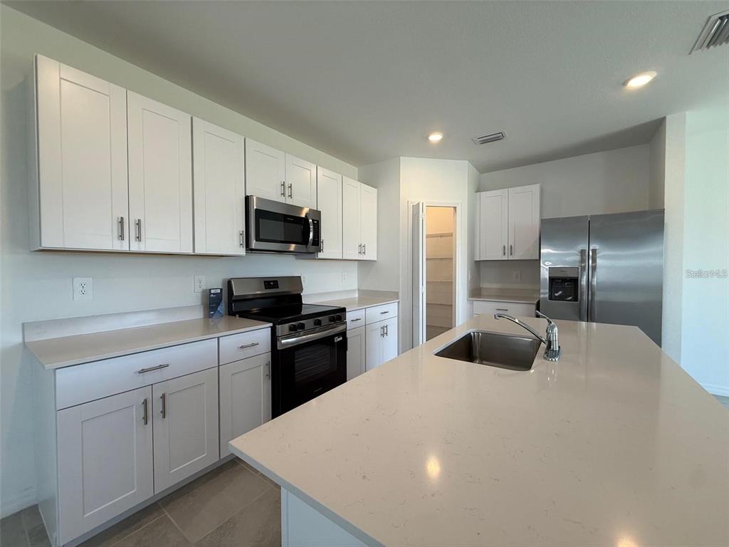A modern kitchen features white cabinets, stainless steel appliances, and a large quartz-topped island — 11795 CLOVERLY LANE, PUNTA GORDA, FL