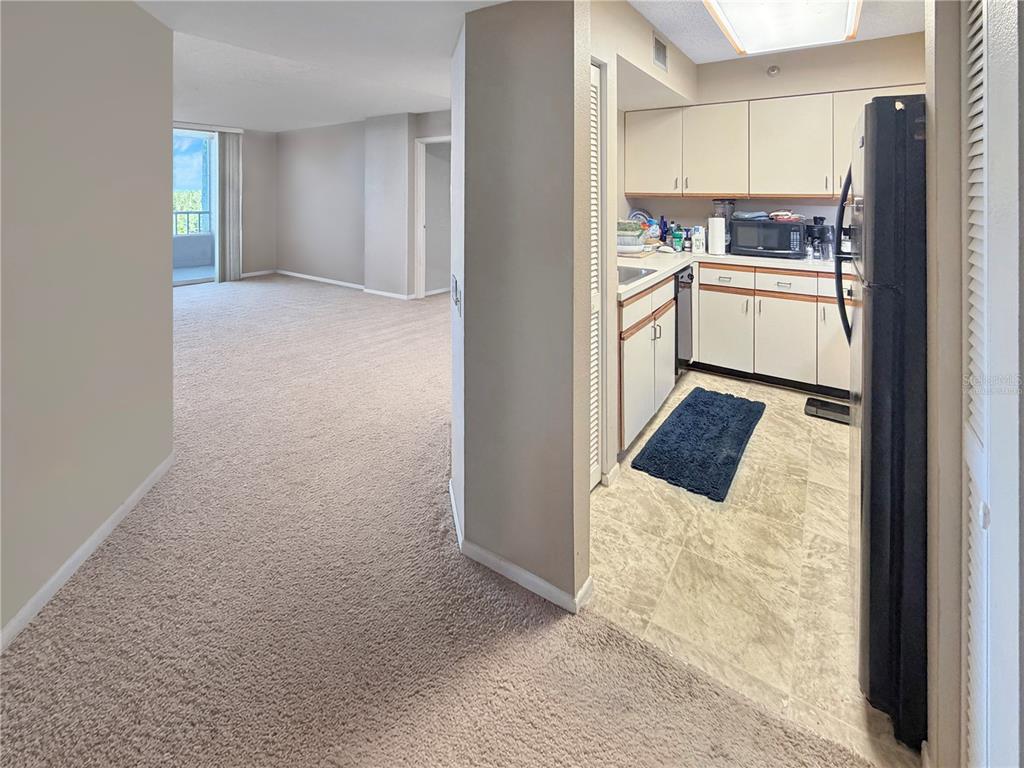 A carpeted living area leads to a kitchen with light cabinets and a black refrigerator — 2333 FEATHER SOUND DRIVE UNIT C507, CLEARWATER, FL