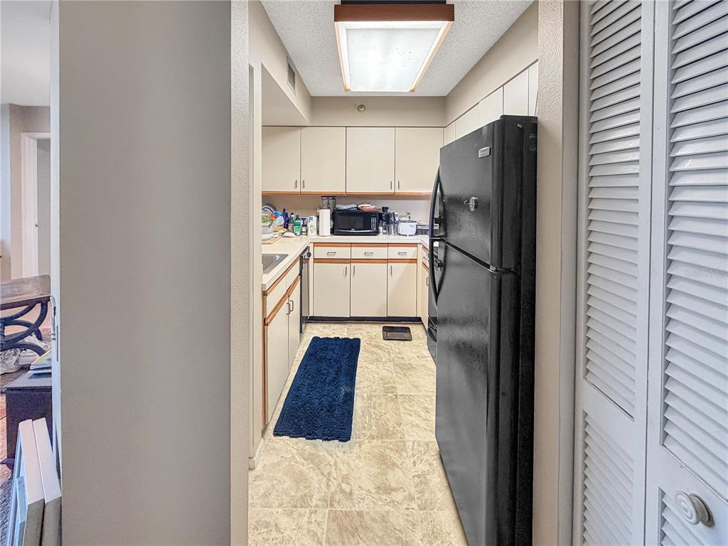 A galley kitchen features light-colored cabinets, a black refrigerator, and a blue floor mat — 2333 FEATHER SOUND DRIVE UNIT C507, CLEARWATER, FL