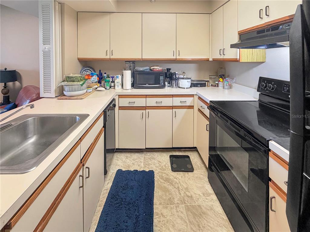 A kitchen features off-white cabinets, laminate countertops, a black stove, and a stainless steel sink — 2333 FEATHER SOUND DRIVE UNIT C507, CLEARWATER, FL