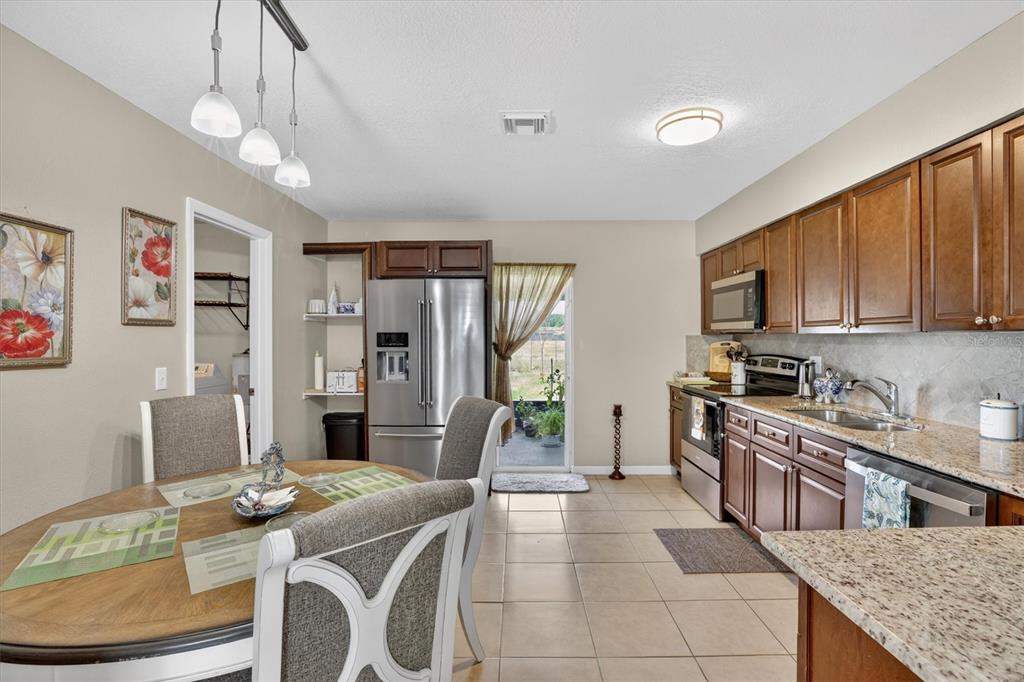 A kitchen and dining area with wood cabinets, granite countertops, and stainless steel appliances — 3804 JANIE COURT, ORLANDO, FL