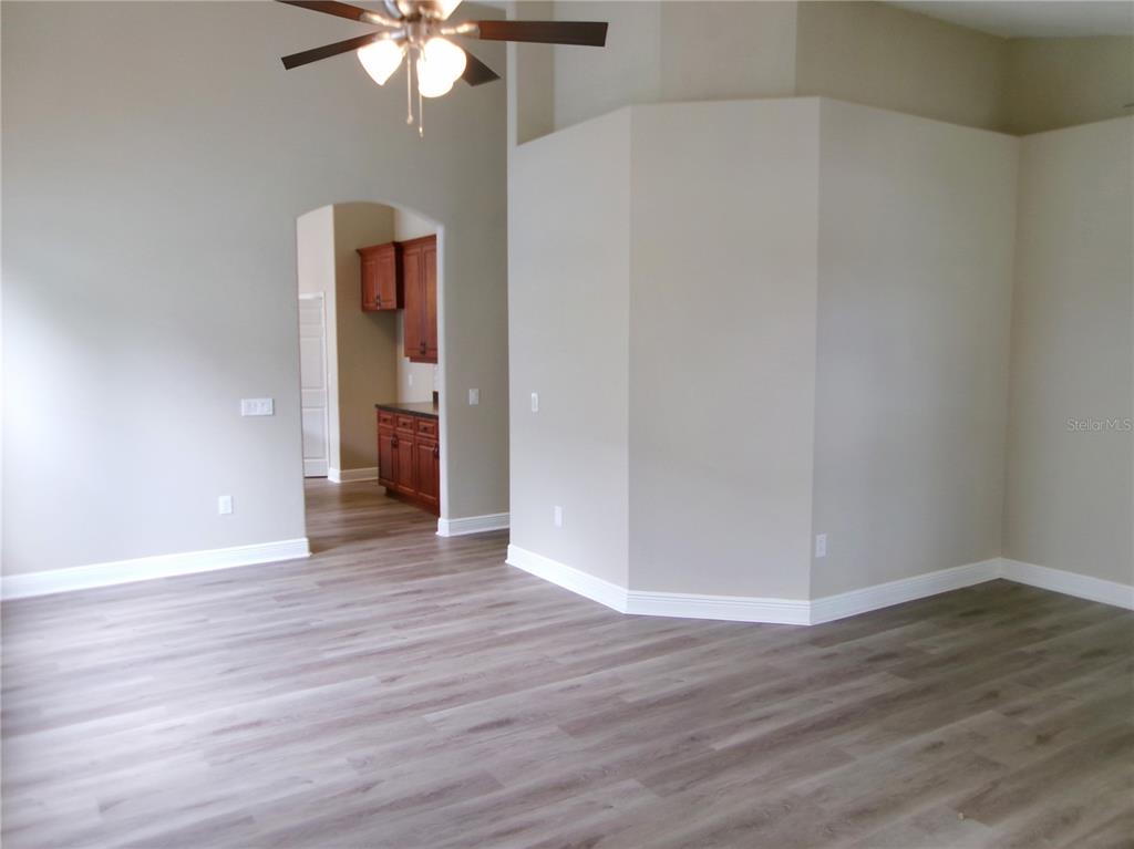 An interior view shows a living area with wood-look flooring leading to a kitchen doorway — 37450 PICKETTS MILL AVENUE, ZEPHYRHILLS, FL
