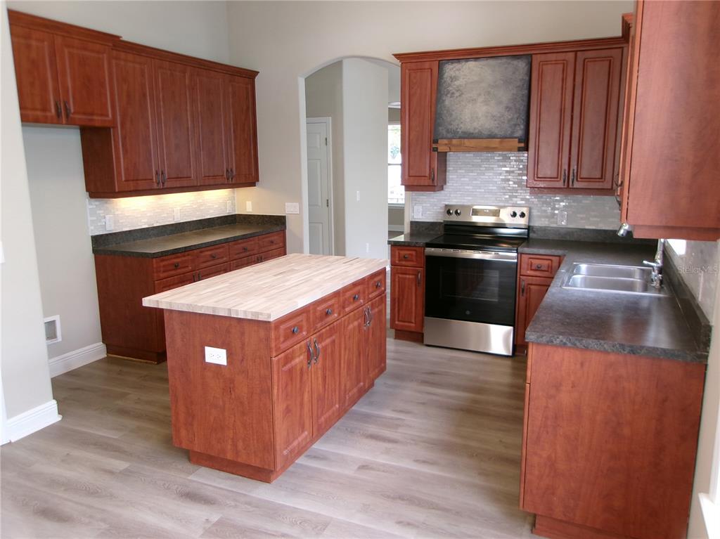 A kitchen features cherry-toned cabinets, a butcher block island, dark countertops, and stainless steel appliances — 37450 PICKETTS MILL AVENUE, ZEPHYRHILLS, FL