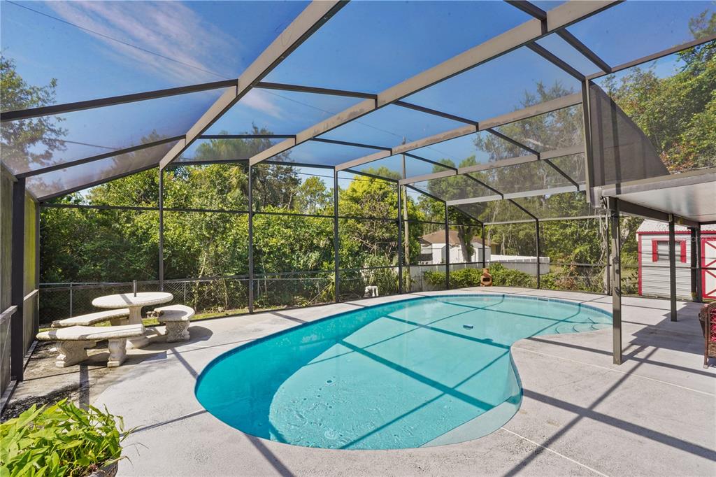 A screened-in patio features a kidney-shaped swimming pool and a stone table with benches — 515 CLOUDCROFT DRIVE, DELTONA, FL